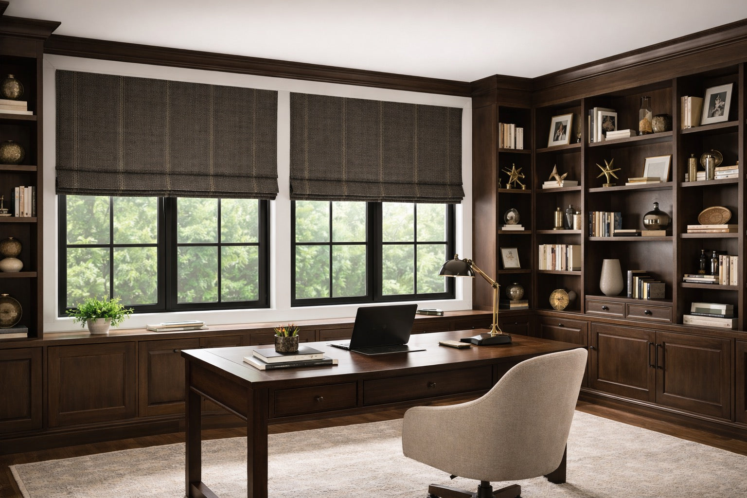 Luxury home office with dark wood built-ins and large black-framed windows featuring custom textured Roman shades in a rich brown woven fabric, styled above a desk with warm lighting and greenery views.